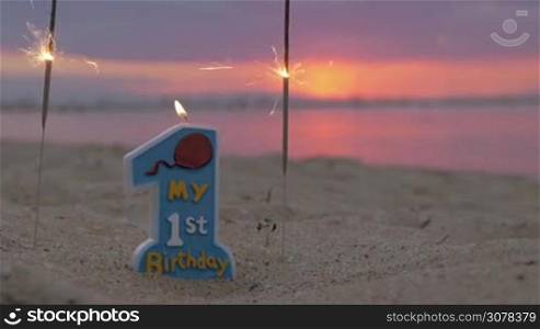 Close-up shot of burning candle and sparklers on the beach at sunset. The first birthday of baby boy