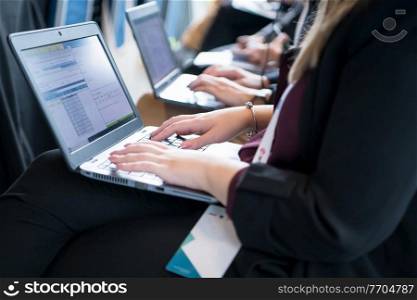 close up shot of business people hands typing on laptop computer keyboard during the business seminar at big modern conference room