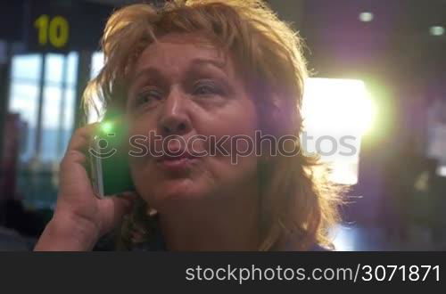 Close-up shot of cheerful senior woman talking on cell phone at the airport terminal