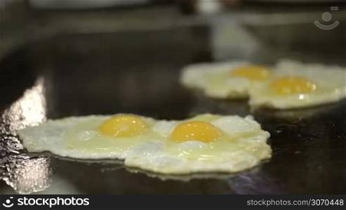 Close-up shot of cooking fried eggs on big flat stove in cafe or restaurant