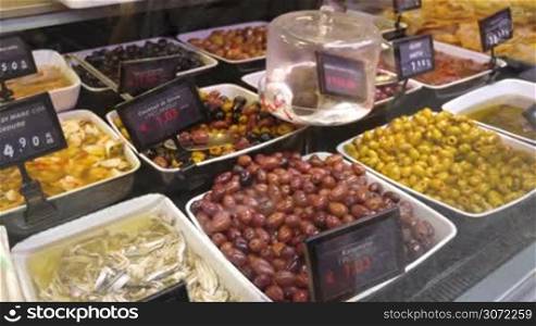 Close-up shot of customer using smartphone to take pictures of olives and seafood presented in the store