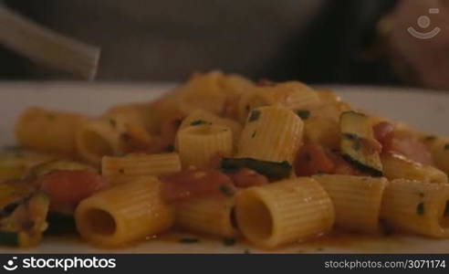 Close-up shot of eating delicious pasta dish with tomato sauce and zucchini. Dinner in cafe or restaurant