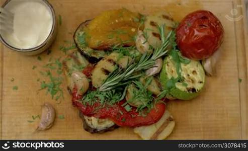 Close-up shot of eating grilled vegetables with cream sauce. Dish served on wooden board, top view