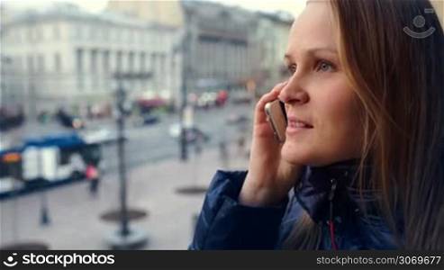 Close-up shot of exciting woman talking on the phone outdoor. Blurry cityscape in background