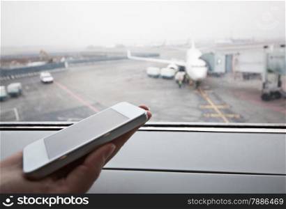 Close-up shot of female hand holding smart phone by window at airport. Area with airplane in background