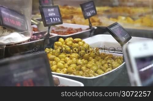 Close-up shot of female hand with smart phone making photo of marinated olives prsesented on shop-display
