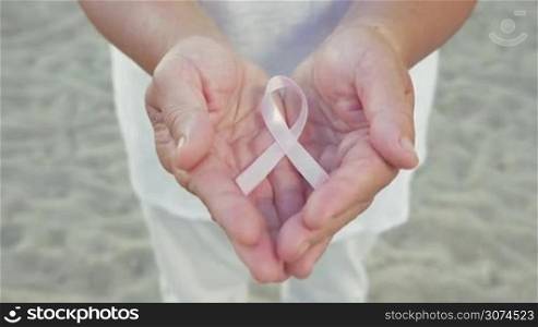 Close-up shot of female hands holding pink ribbon outdoor. Breast cancer awareness ribbon