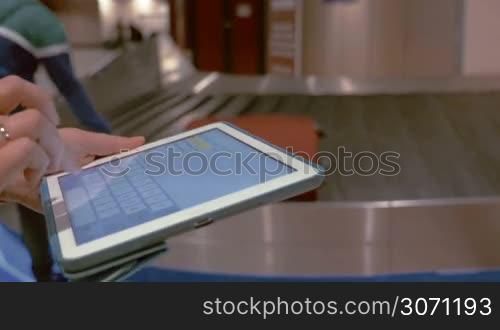 Close-up shot of female hands typing message on tablet PC near the baggage claim at the airport