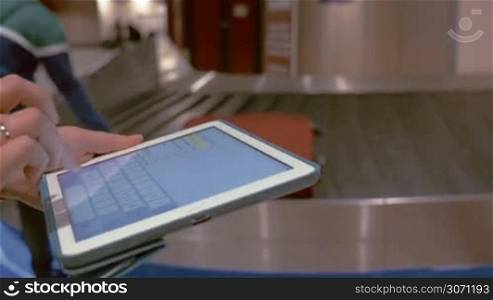 Close-up shot of female hands typing message on tablet PC near the baggage claim at the airport