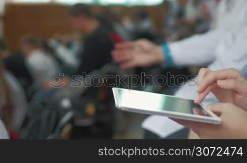 Close-up shot of female hands typing on tablet computer in auditorium during the medical lecture, conference or symposium