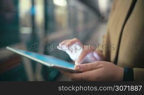 Close-up shot of female hands typing on touch pad near the leaving train at underground station. Easy way to work to communicate in any place