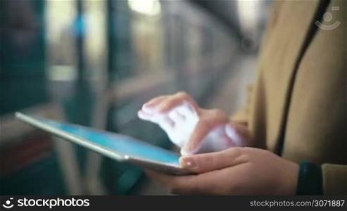 Close-up shot of female hands typing on touch pad near the leaving train at underground station. Easy way to work to communicate in any place