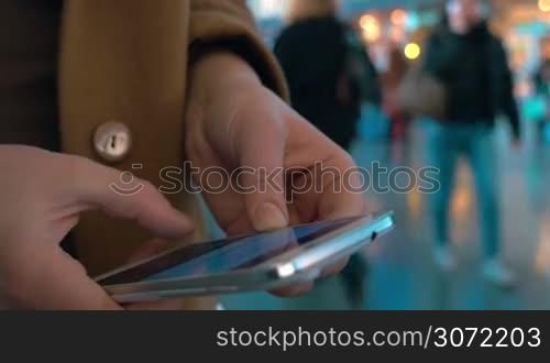 Close-up shot of female hands typing sms or chat message on smart phone at the station or airport. Defocused background with walking people
