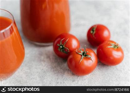 Close up shot of four ripe red tomatoes on white background, fresh juice in glasses near. Healthy lifestyle. Delicious drink made of vegetables