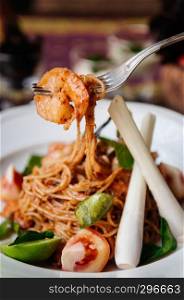 Close up shot of Fusion spaghetti shrimp pasta with Thai Tom Yum Gung spicy sauce, kaffir lime leaves, lemongrass and tomatoes