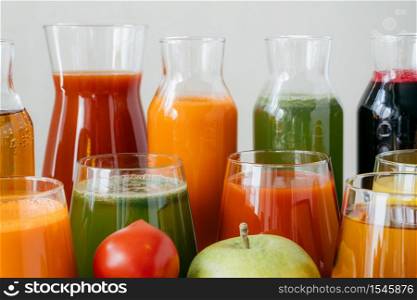 Close up shot of glass bottles filled with colorful juice made of various vegetables and fruit, red tomato and green apple in foreground. Fresh detox drink