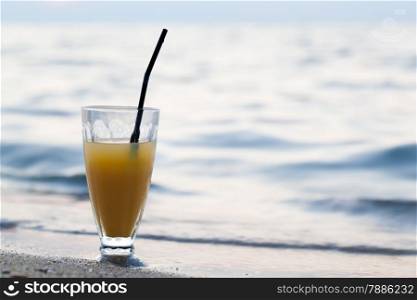 Close-up shot of glass of cocktail or fruit juice with straw standing on beach close to sea. Summer vacation