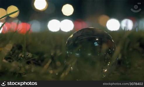 Close-up shot of glass sphere on roadside grass with traffic in background. Shot in the night city