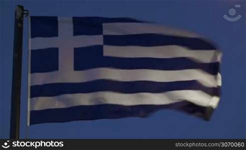 Close-up shot of Greek flag waving in strong wind against evening sky