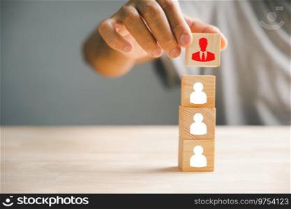 Close-up shot of hand selecting man people icons on cube wooden toy blocks stacked. Illustrates the concept of employee management and the importance of human resources in business success.. A red manager icon that stands out distinctively from a group of staff employee icons displayed