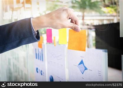 Close up shot of hands of business man sticking adhesive notes on glass wall in office.