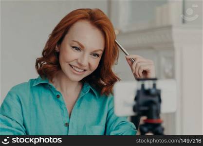 Close up shot of happy redhead woman records video on webcam, talks to subscribers, has personal blog, gives advice, makes live broadcast or fims webinar. Online teacher records vlog teaches languages