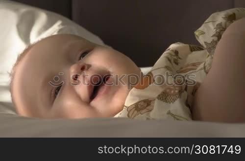 Close-up shot of lovely smiling blue-eyed baby girl of six months old lying on bed at home