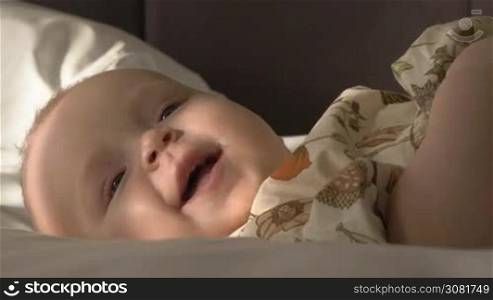 Close-up shot of lovely smiling blue-eyed baby girl of six months old lying on bed at home