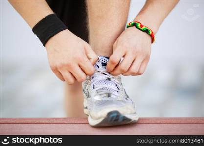 Close-up shot of man tying running shoes with foot on the bench. Getting ready before jogging. Going in for sports, healthy lifestyle