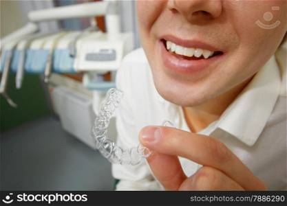 Close-up shot of man with big smile holding mouth guard or orthodontic retainers in dental office