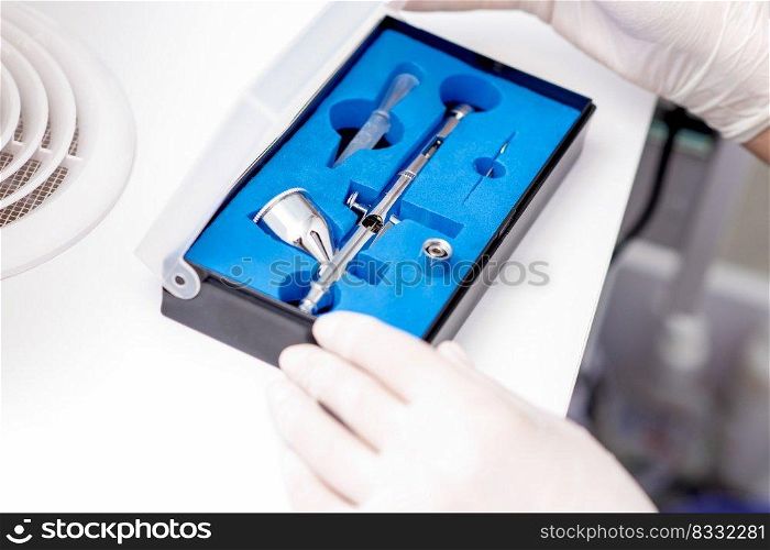 Close up shot of manicure master hand is taking out new clean airbrush tool for nails wearing gloves from the blue box. Manicure master taking out airbrush tool