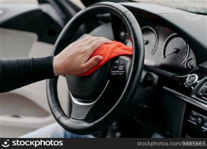 Close up shot of mans hand cleaning car steering wheel with microfiber cloth. Hygiene prevention during coronavirus outbreak