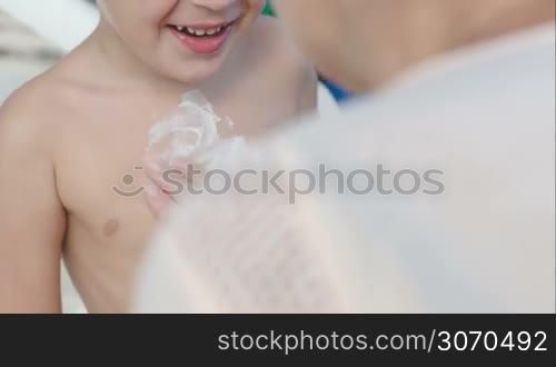 Close-up shot of mother applying sunscreen on sons chest, she making the sun with cream strokes