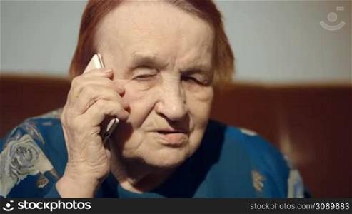 Close-up shot of old woman talking on the cell phone at home