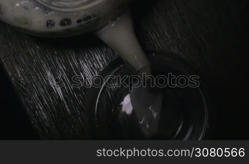 Close-up shot of pouring Indian masala tea from glass tea-pot into a tea bowl. Top view