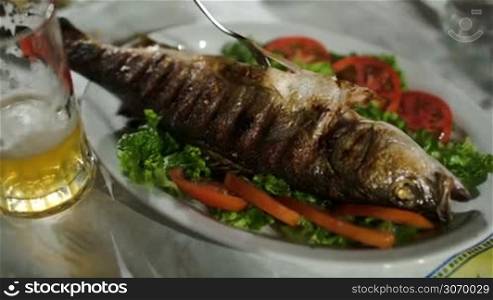 Close-up shot of pouring sauce on fried fish served with green salad and tomatoes