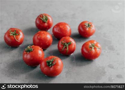 Close up shot of red tasty heirloom tomatoes with green leaves and water droplets harvested from garden isolated over grey background.