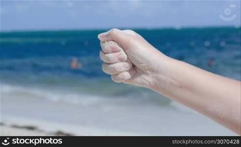 Close-up shot of sand pouring from female hand on blue sea background