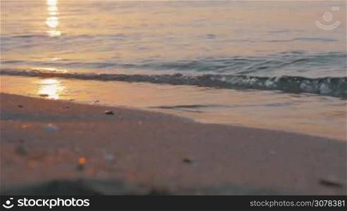 Close-up shot of sea waves washing the shore at sunset. Golden sun reflection in water