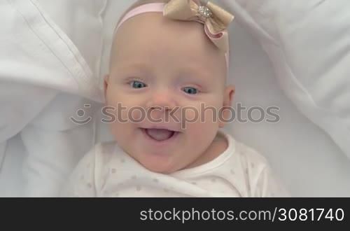 Close-up shot of six months old baby girl with a bow. Portrait of happy blue-eyed child lying on bed