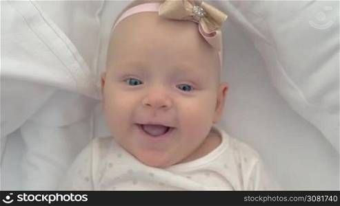 Close-up shot of six months old baby girl with a bow. Portrait of happy blue-eyed child lying on bed