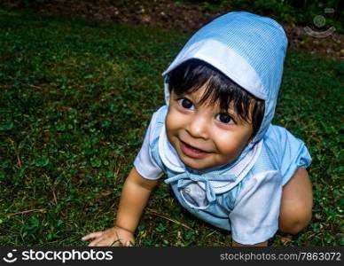 Close up shot of smiling latino baby dressed up and crawling outside in the grass
