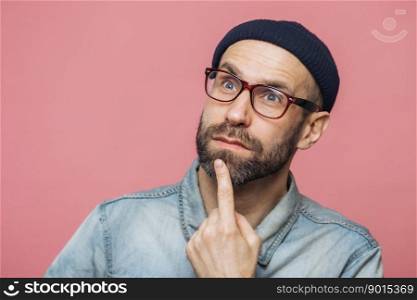 Close up shot of thoughtful bearded male with blue eyes being deep in thoughts, looks pensively into distance, ponders about something, isolated over pink background. Attractive man poses indoor