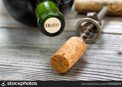 Close up shot of top of wine bottle cork, focus on the words enjoy, with rustic opener in background. Horizontal format layout.