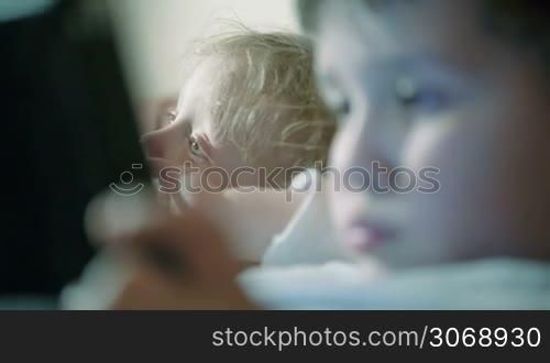 Close-up shot of two brothers with changing focus. One kid watching TV, the other using touchpad