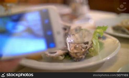 Close-up shot of using smartphone to take photo of fresh oysters served in restaurant