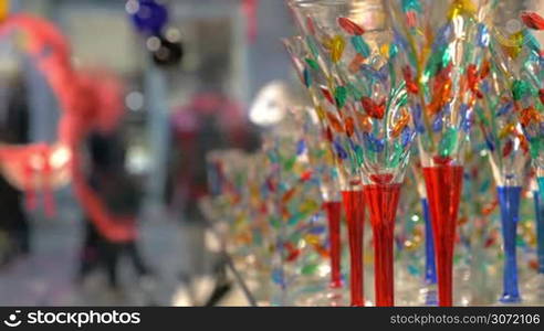 Close-up shot of wineglasses in the store decorated with colorful elements. Beautiful and famous Venetian glass. People walking in the street in background