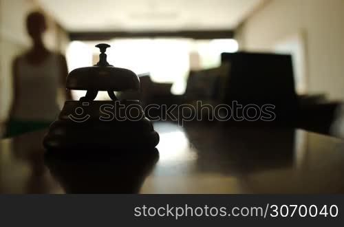 Close-up shot of woman coming up to hotel counter desk and ringing reception bell