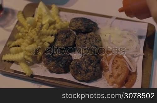 Close-up shot of woman dining with meat patties, fried potatoes, fresh tomatoes and onions