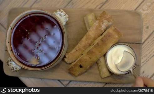 Close-up shot of woman eating borscht with sour cream and bread served on wooden board in restaurant